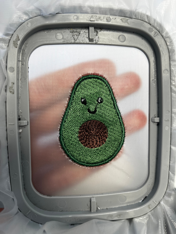 Fertig mit Satin Stich umrandete Avocado, noch auf dem jetzt an der Kante perforierten Stickvlies