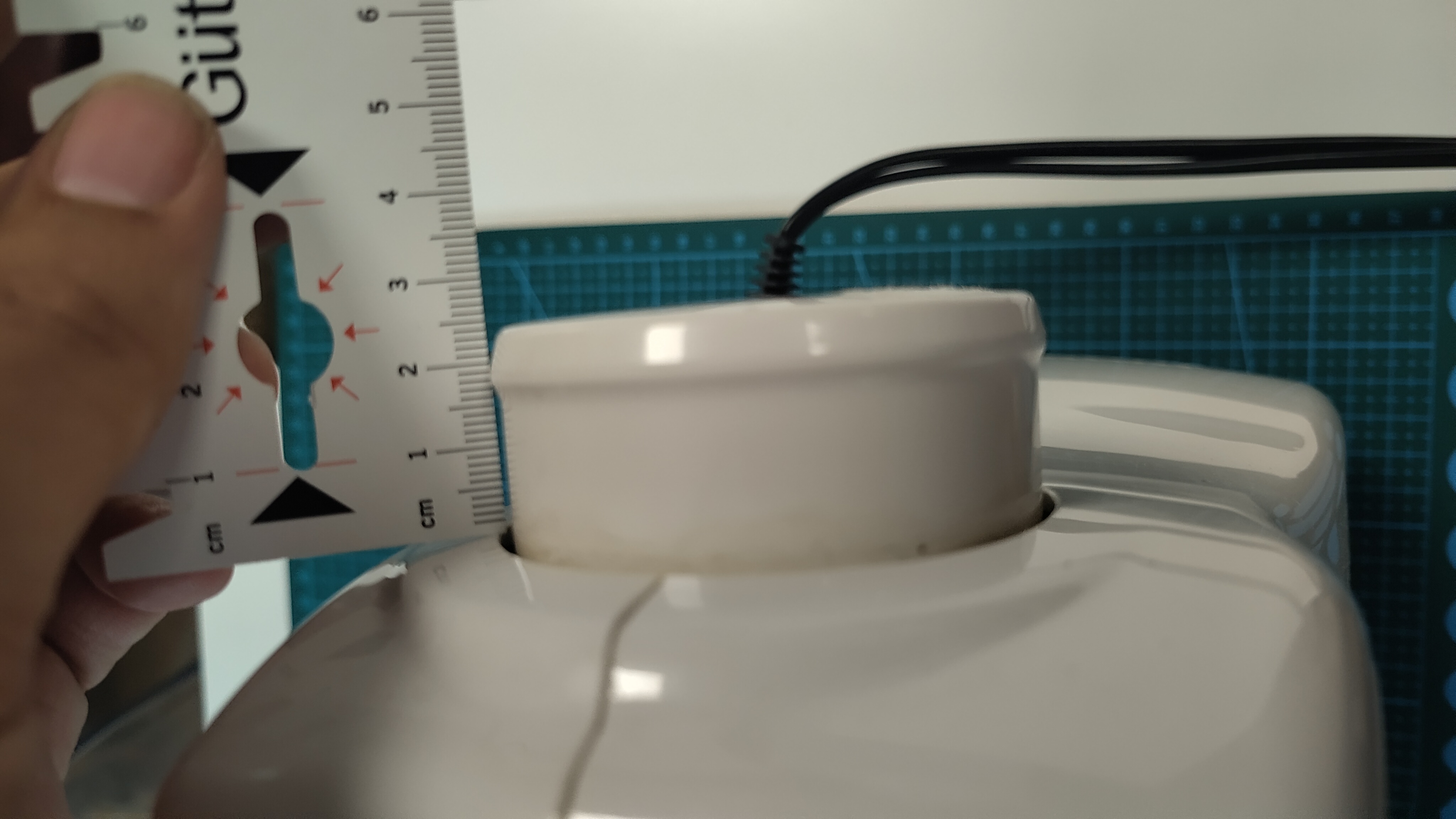 Die Handkurbel der Nähmaschine ist zu sehen, daneben ein Lineal, sie ist circa 2,5cm abstehend vom Gehäuse